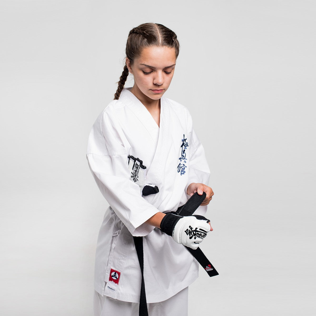 Athlete wearing white karate gi putting on black and white Gants Kyokushin FUJIMAE martial arts gloves.