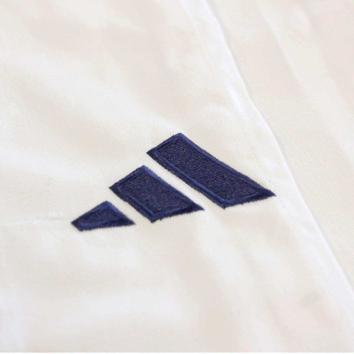 Kimono de judo Adidas Replica blanc avec logo brodé bleu, tissu résistant grain de riz pour compétitions IJF.