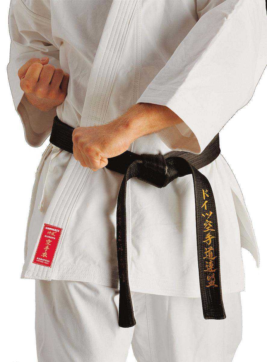 Close-up of a person wearing a white Kimono Karate Kamikaze Europa with black belt tied at the waist, highlighting the red label on the jacket.