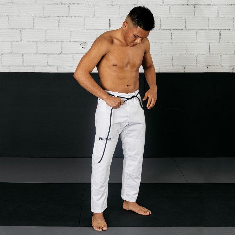 Man wearing white FUJIMAE Jiu Jitsu training pants adjusting waist tie on mat