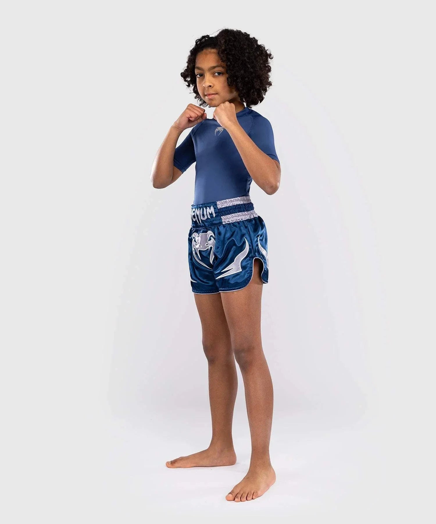 Child wearing blue Short Muay Thai Venum Inferno with elastic waistband and side slits in fighting stance