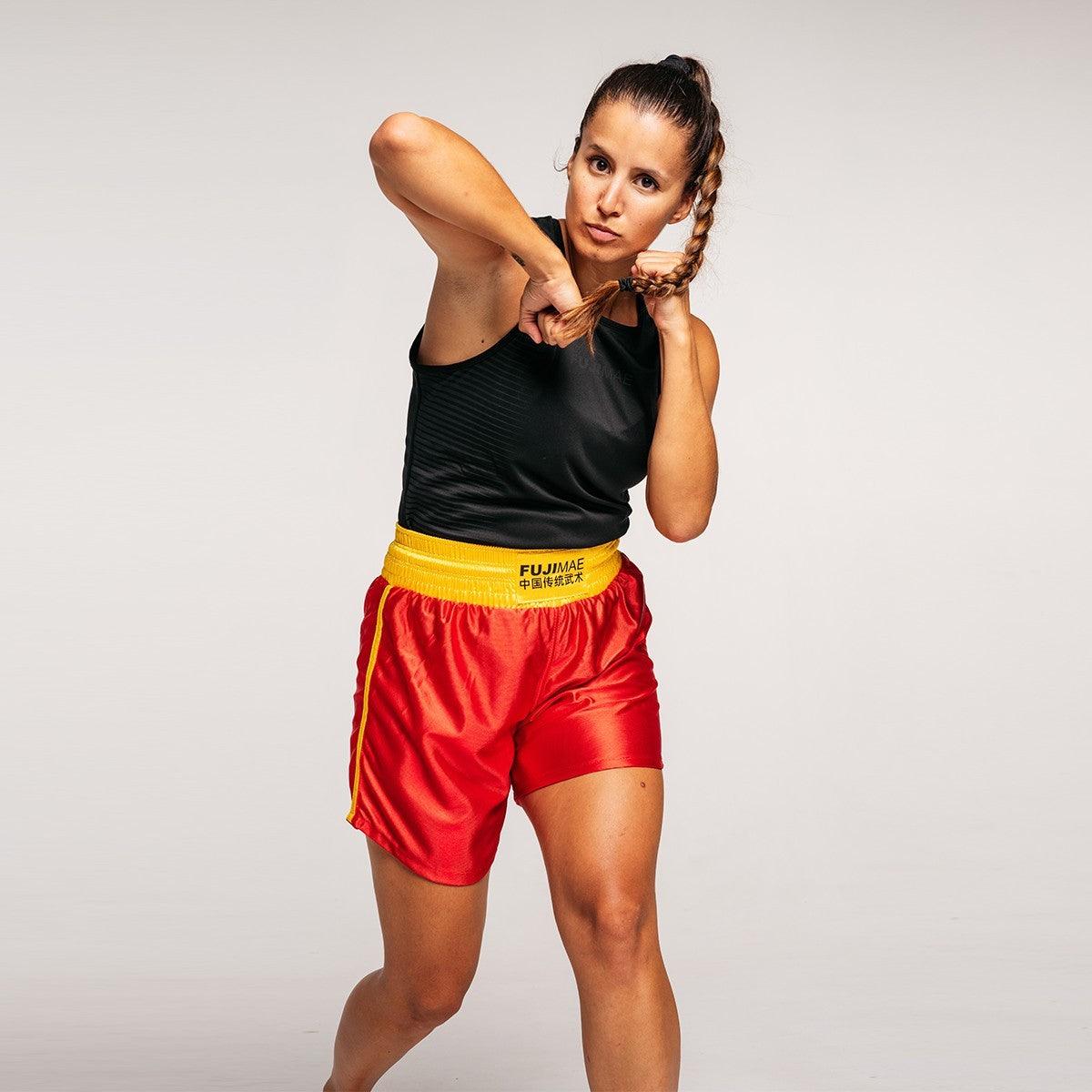 Female athlete wearing red and yellow FUJIMAE Sanda training shorts in a fighting stance