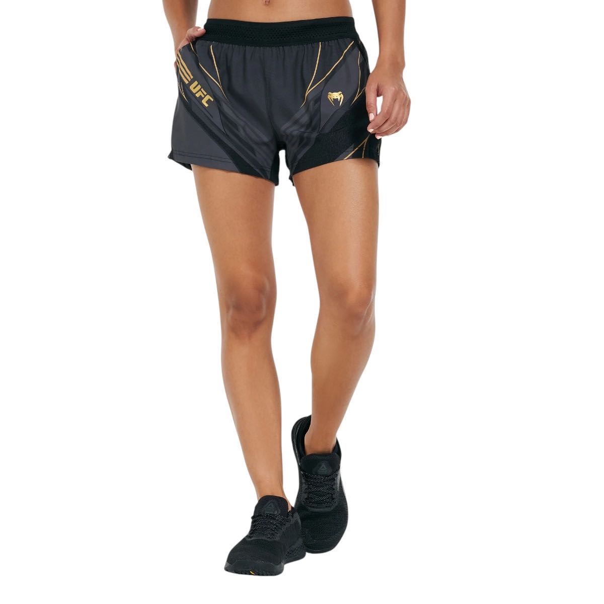 Women's UFC Venum Replica Champion sports shorts in black and gold with elastic waistband and zippered pockets, designed for lightweight and breathable performance.
