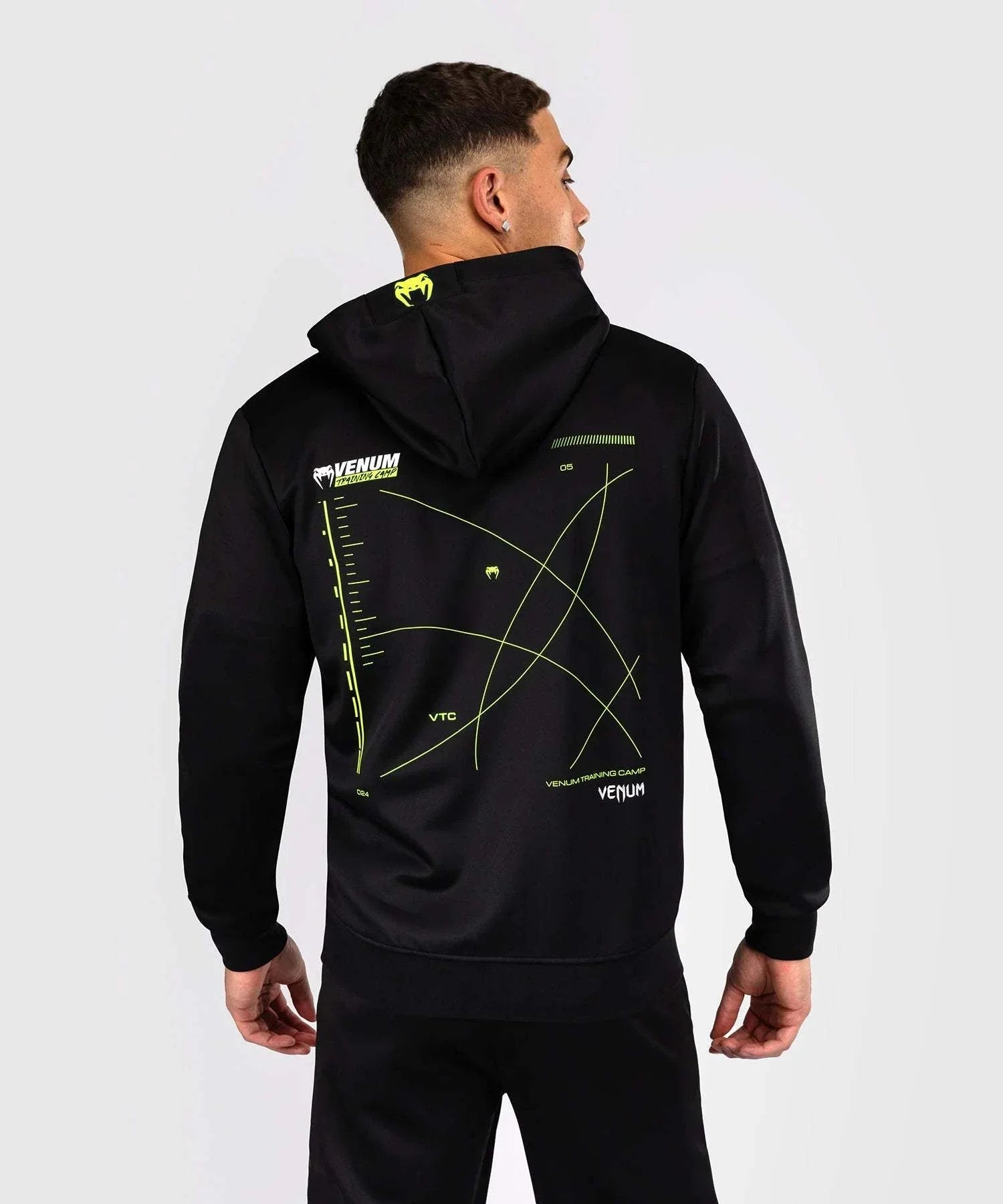 Back view of a man wearing black Venum Training Camp 4.0 zip-up hoodie with neon green graphic accents and adjustable hood.