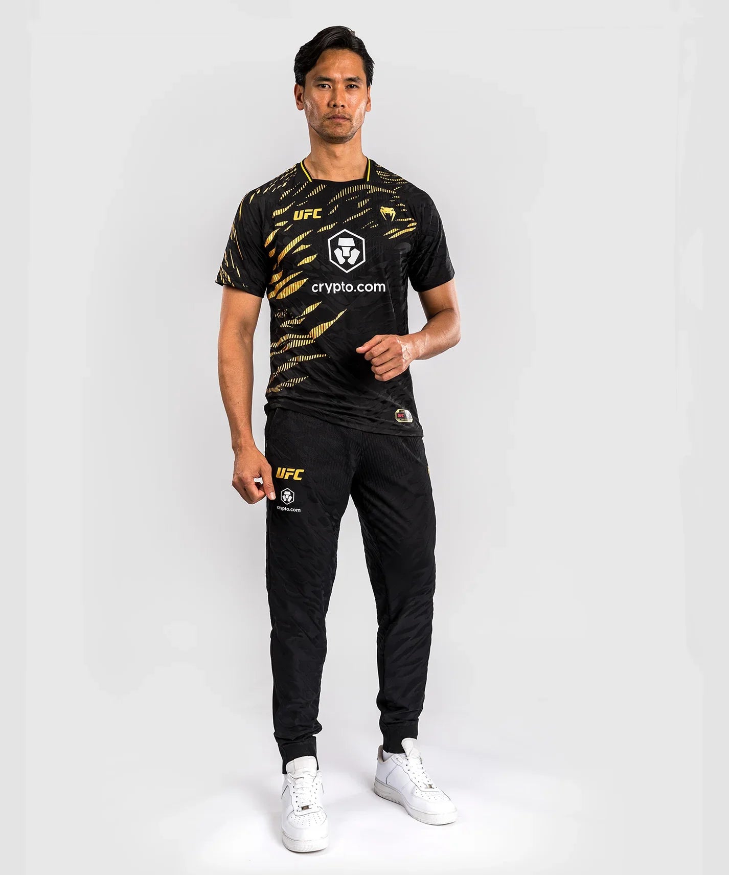Male model wearing black and gold UFC Fusion par Venum Dry-Tech performance T-shirt with short sleeves and printed logos.