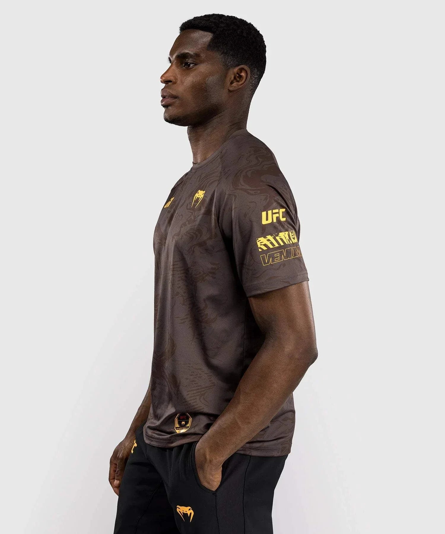 Man wearing brown UFC Fusion by Venum Dry-Tech T-shirt with yellow logos and short sleeves, side view