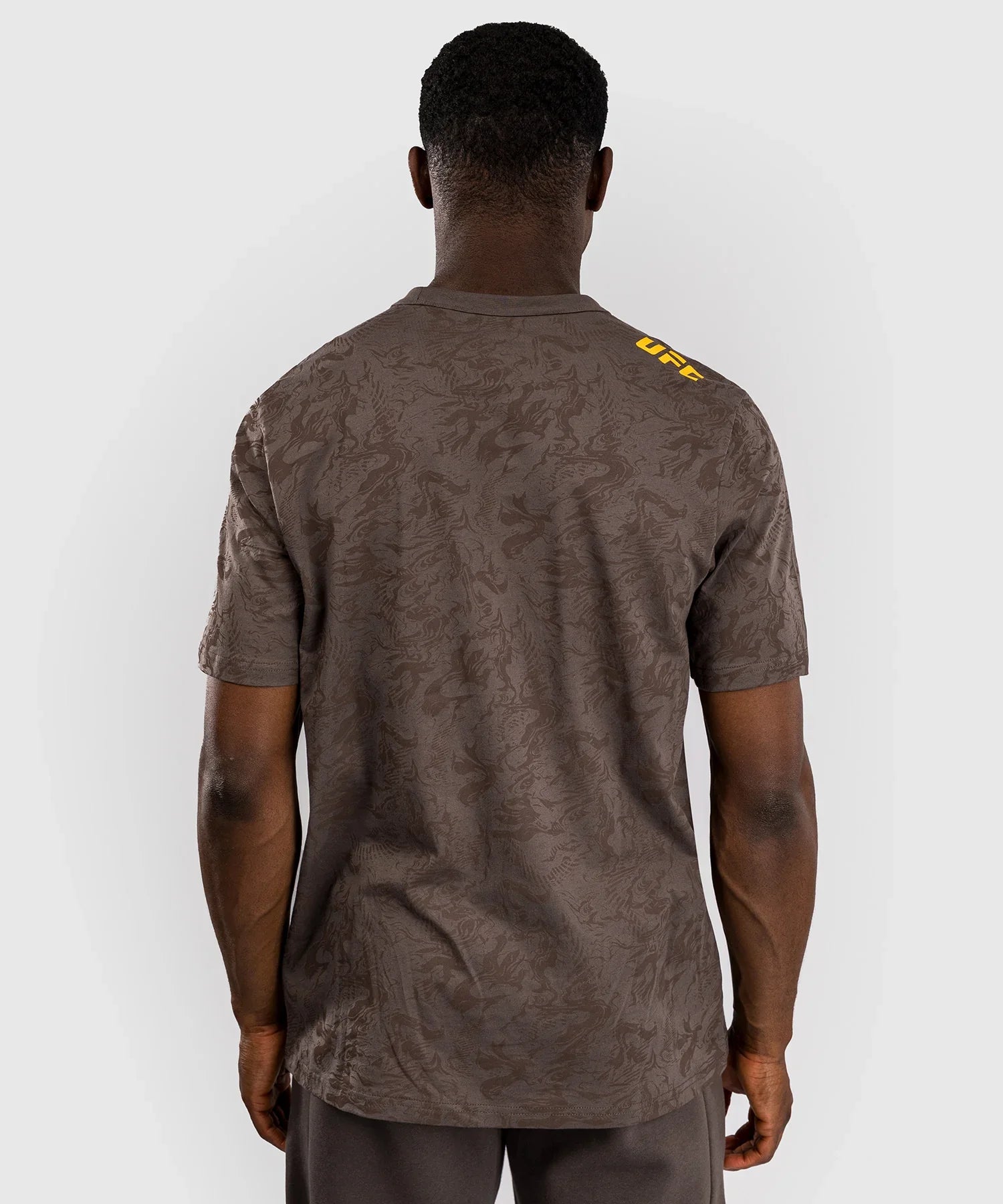 Back view of man wearing brown UFC Fusion par Venum authentic fight week T-shirt with subtle pattern and yellow UFC logo on shoulder