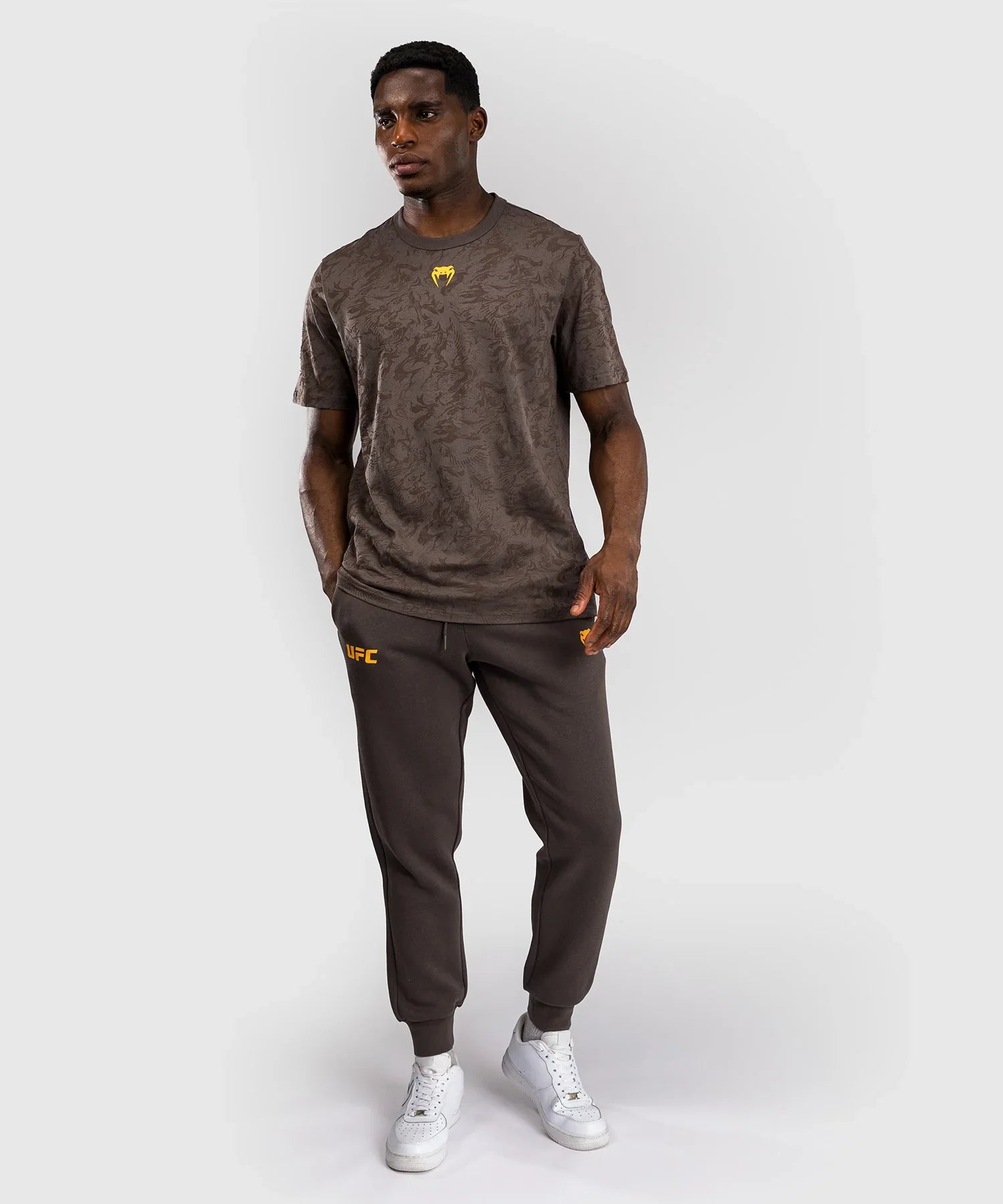 man wearing UFC Fusion by Venum dark brown short sleeve cotton t-shirt with logo and matching joggers and white sneakers