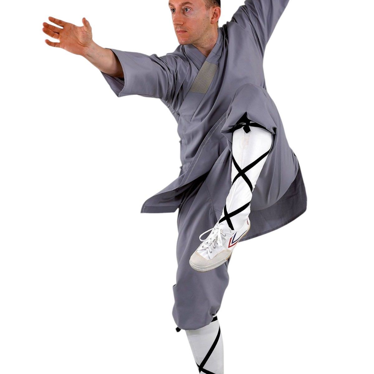Man practicing Kung Fu wearing traditional gray Tenue de Moine Shaolin martial arts uniform with white leg wraps and sneakers