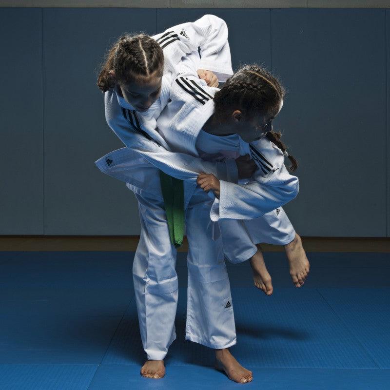 Two young judokas wearing white Kimono Judo Adidas with black shoulder stripes practicing judo on blue mats
