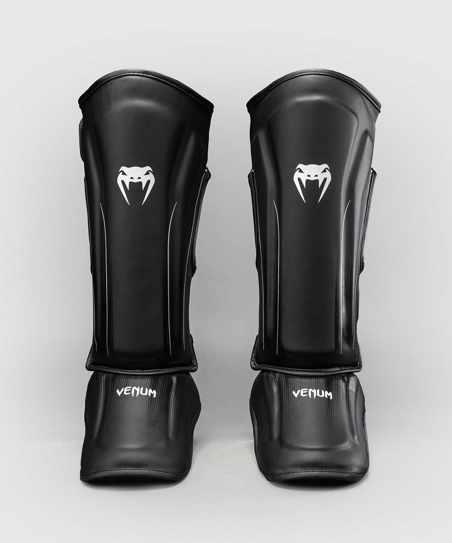 Protège-tibias Venum Stealth noir et blanc pour kickboxing et MMA, coque anatomique avec mousse multi-densité et triple fermeture.