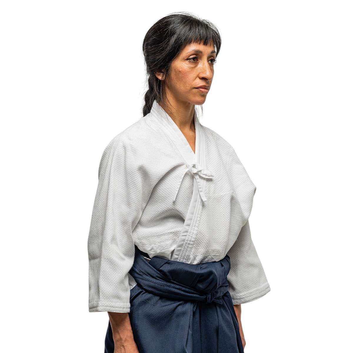 Woman wearing white Fujimae Keikogi Aïkido training jacket with a feminine cut and navy belt isolated on white background