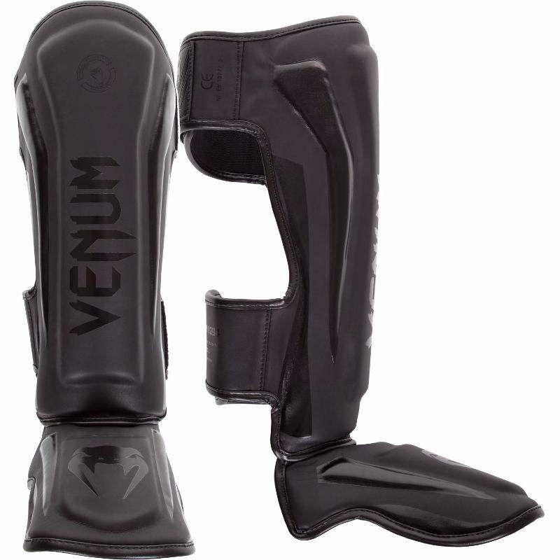 Black Venum Elite shin guards made from premium Skintex leather with ergonomic design and velcro straps for secure fit in Muay Thai and kickboxing.