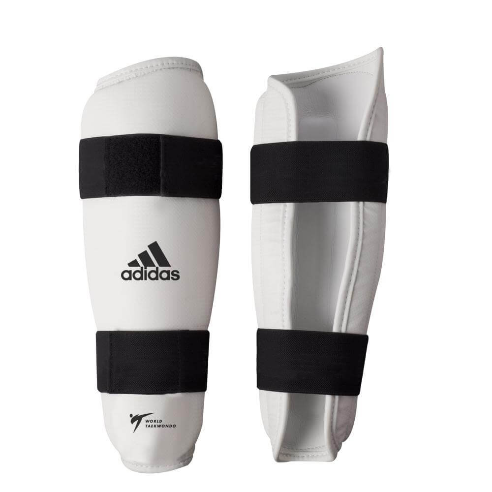 White Adidas Protège-tibias Taekwondo WT shin guards with black double velcro straps, ergonomic design, and World Taekwondo logo
