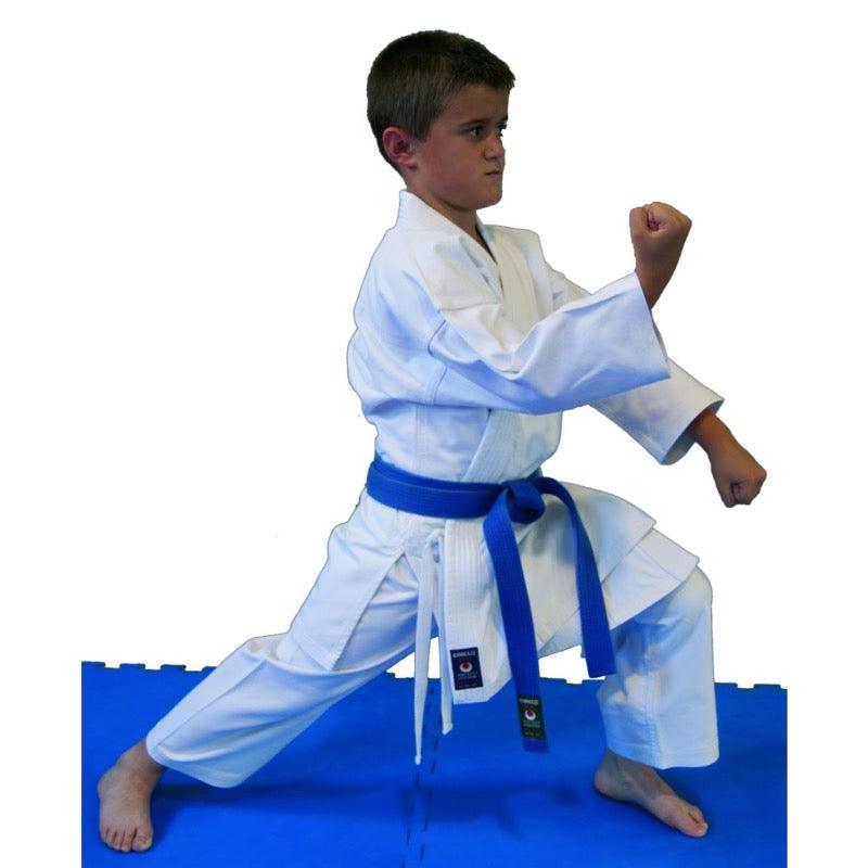 Child wearing white Kimono de Karaté initiation Komodo - Kamikaze with blue belt in karate stance on blue mat