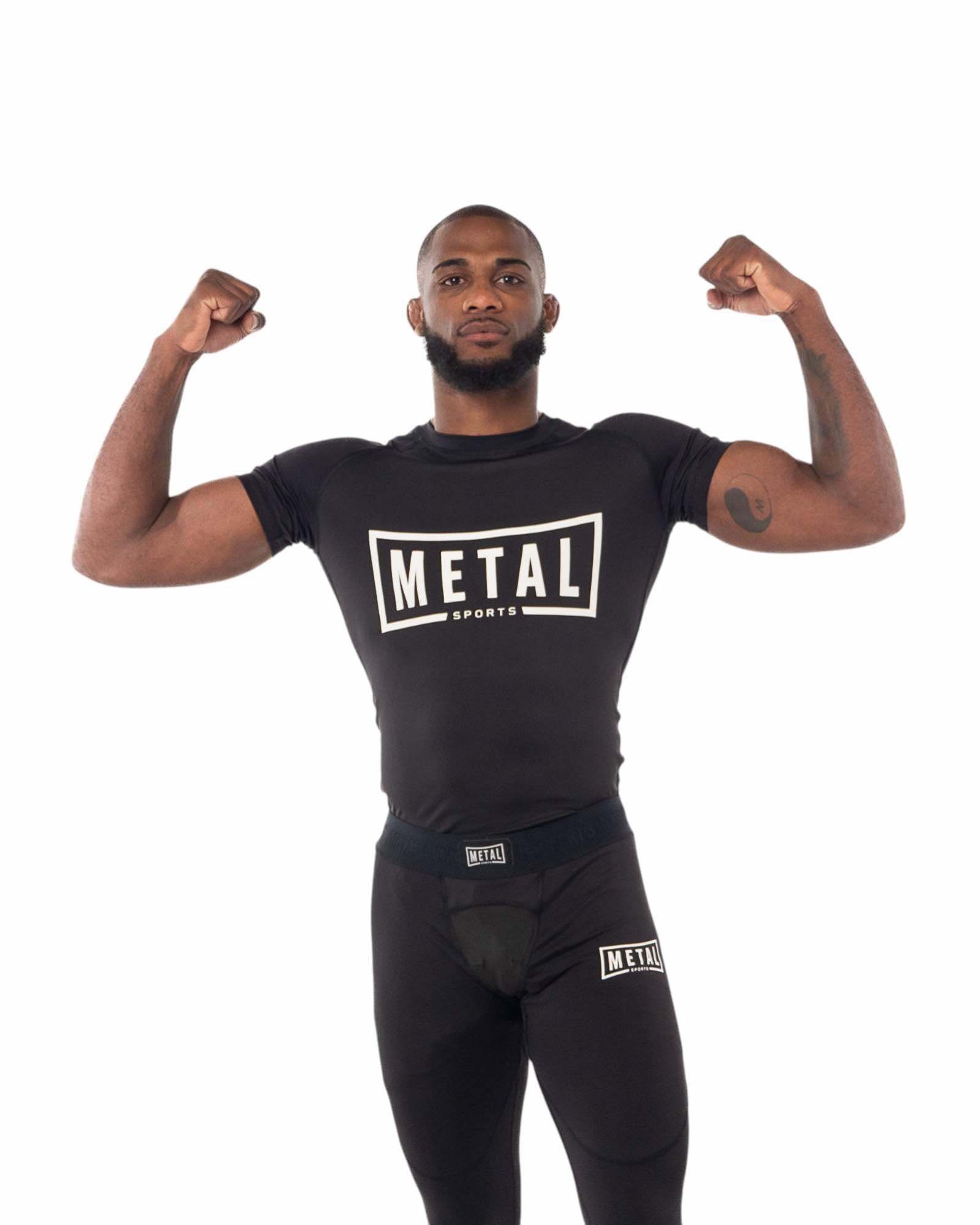 Homme portant un rashguard noir Rashguard One Metal Boxe MSR201N à manches courtes avec logo Metal Sports, posant avec les bras musclés levés.